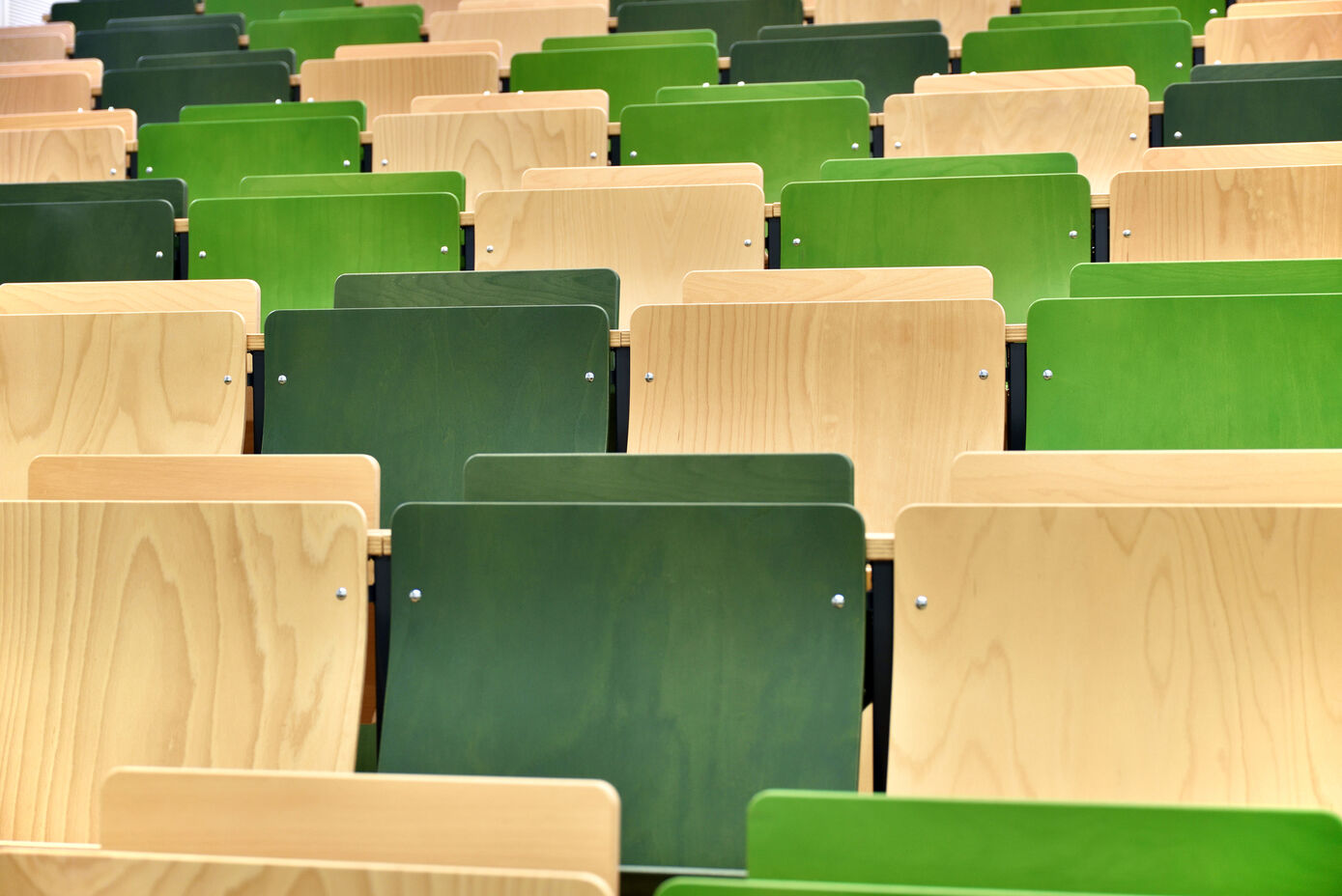 Symbolbild für ein Studium: Hörsaal. Das Bild zeigt einen Ausschnitt der Bestuhlung in einem Hörsaal. Die Stühle sind hell- und dunkelgrün sowie holzfarben.