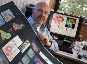 Prof. Dr. Ferdinand von Eggeling mit einem Poster, auf dem die Technologie der bildgebenden Massenspektrometrie erklärt wird. Foto: Jan-Peter Kasper/FSU