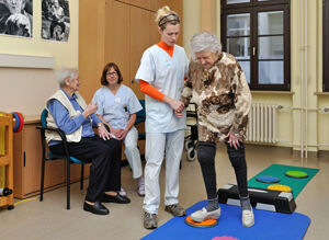 Unter Anleitung und Hilfe einer Sporttherapeutin absolviert eine Patientin ein Gleichgewichtstraining, das zur aktivierenden Therapie in der Tagesklinik der Klinik für Geriatrie gehört. Foto: M. Szabo/UKJ