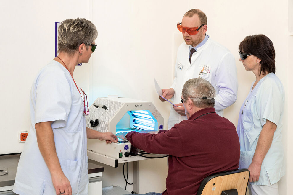 Oberarzt Dr. Steven Goetze mit den Pflegeassistentinnen Heike Lenk (links) und Ines Bertling bei der Behandlung eines Handekzems mit einer Creme-PUVA-Therapie. Foto: UKJ/Hellmann