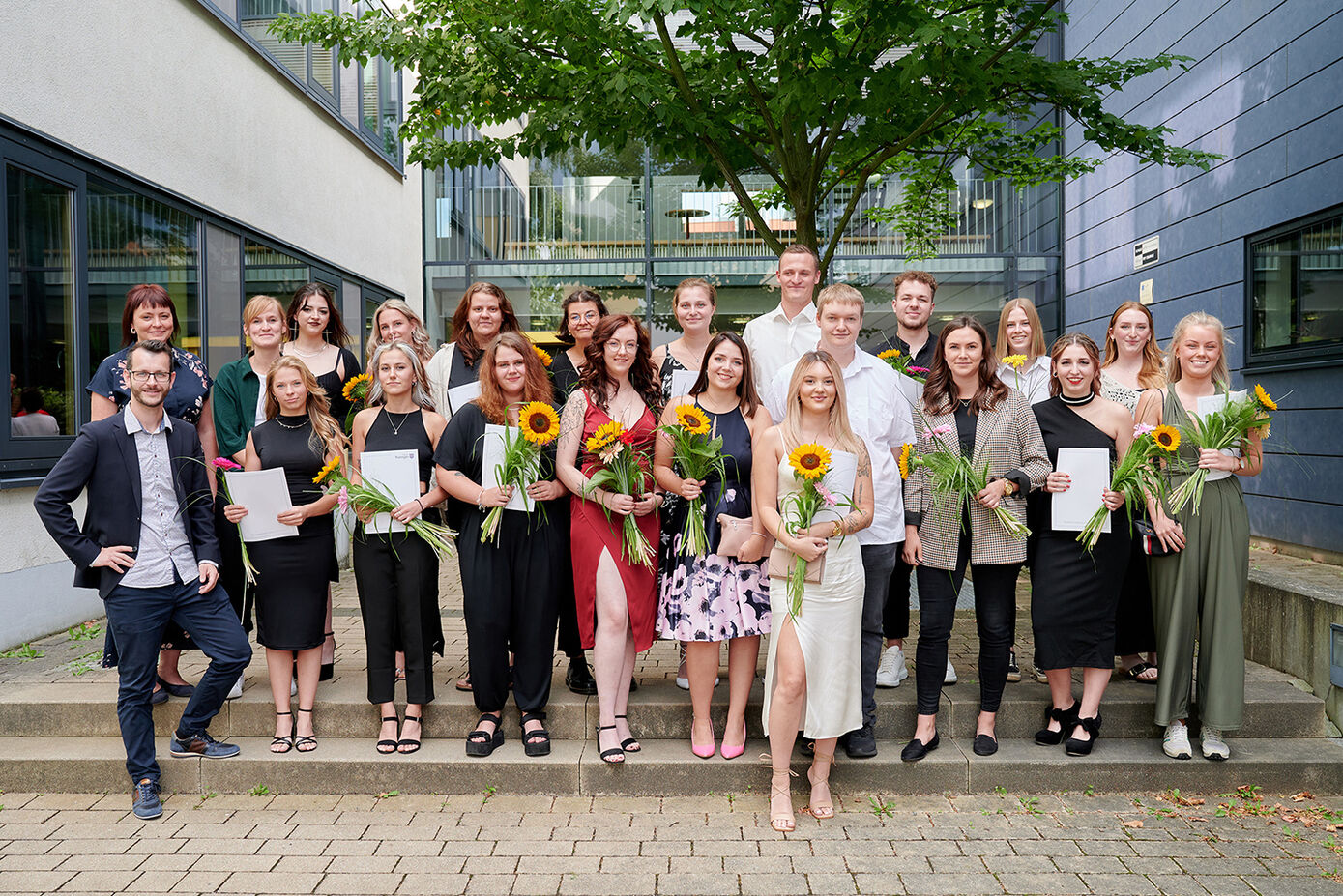 Freudestrahlend halten die Absolventinnen und Absolventen der generalistischen Pflegeausbildung am Universitätsklinikum Jena Zeugnisse und Sonnenblumen in den Händen. (Foto: UKJ/Hellmann)