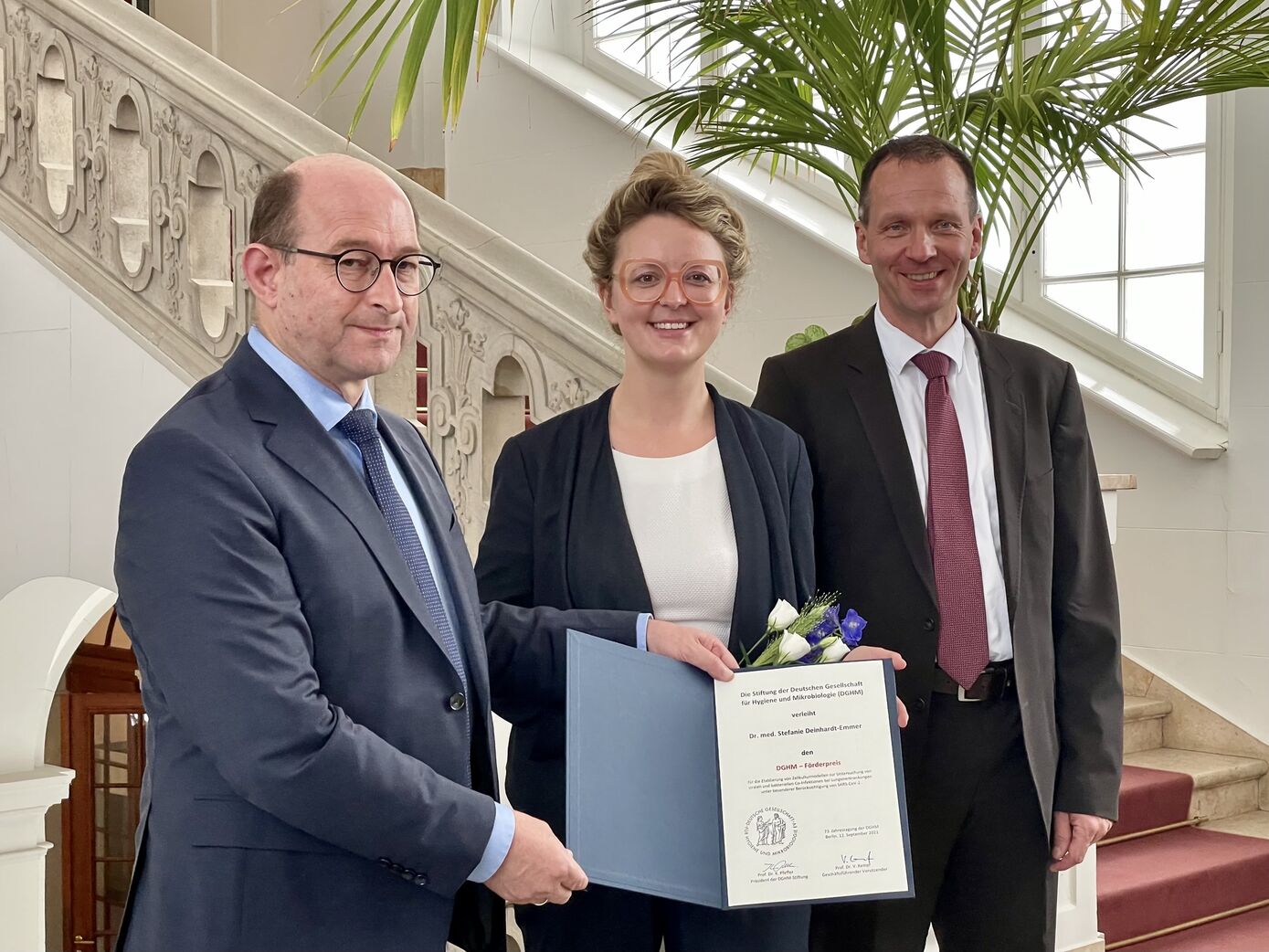 Prof. Klaus Pfeffer (l.) und Prof. Volkhard Kempf (r.) von der Stiftung der Fachgesellschaft übergeben den Förderpreis an Dr. Stefanie Deinhardt-Emmer. Foto: DGHM