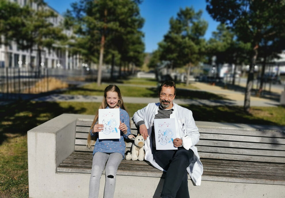 Yaël und Dr. Karim Kentouche, Oberarzt der Kinderklinik des Universitätsklinikums Jena, halten stolz die Geschichte von „Kuh-Linda in der Röhre“ in den Händen. Foto: UKJ/Korneli